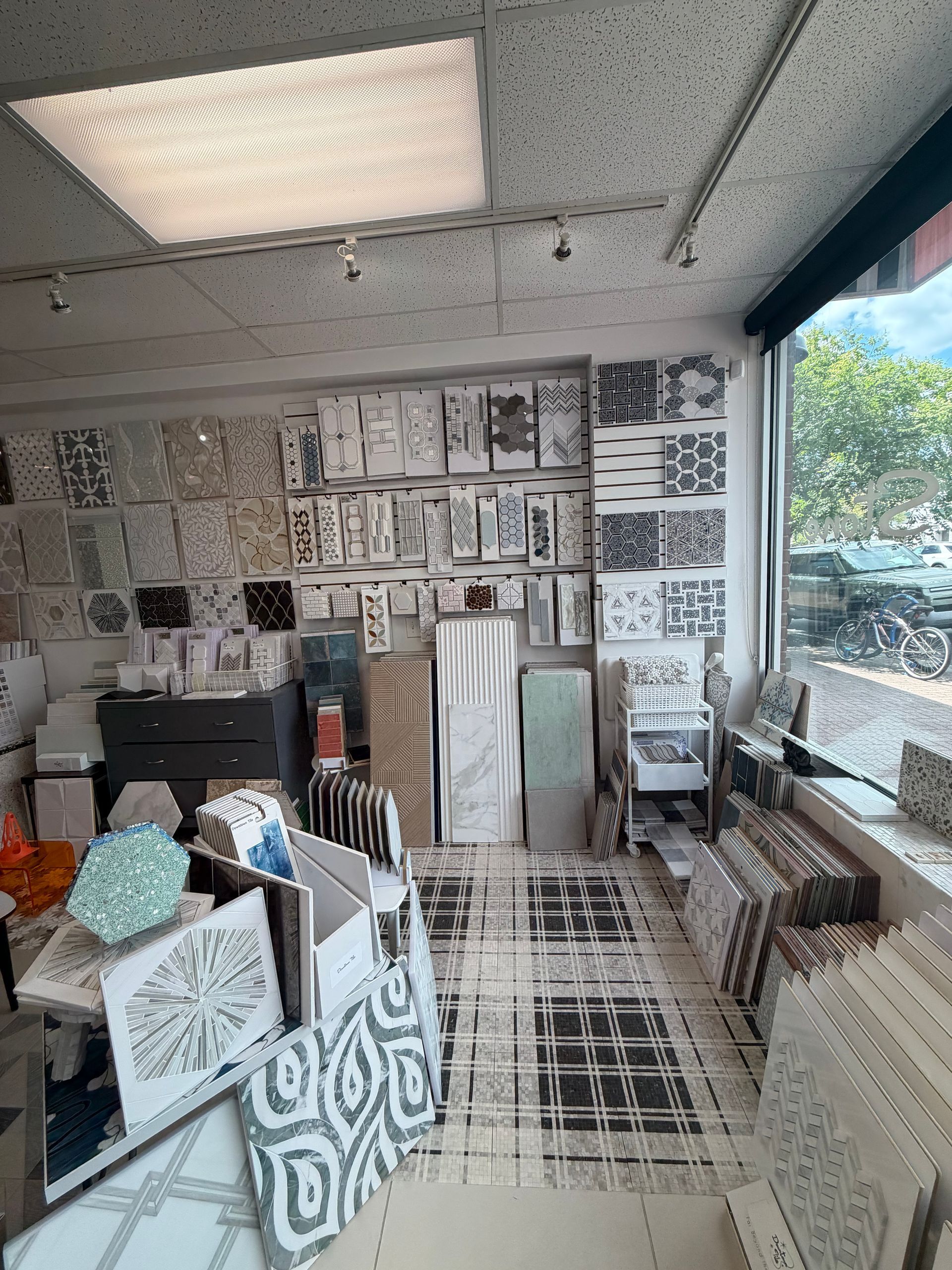 Art studio with patterned wall tiles, shelves of ceramics, and a large open window overlooking trees