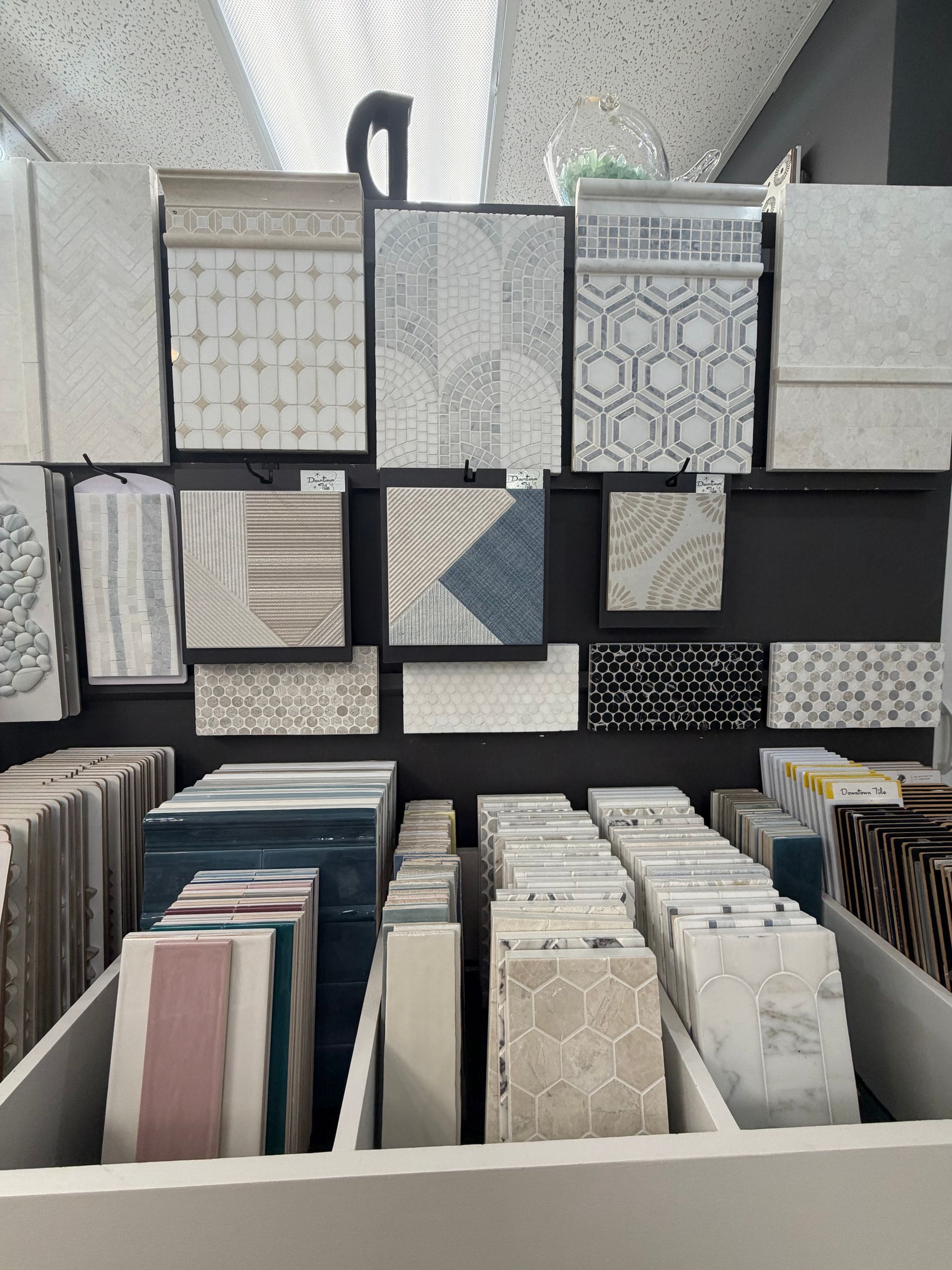 Patterned wallpaper and tile samples displayed in a store rack, with sample books in the foreground.