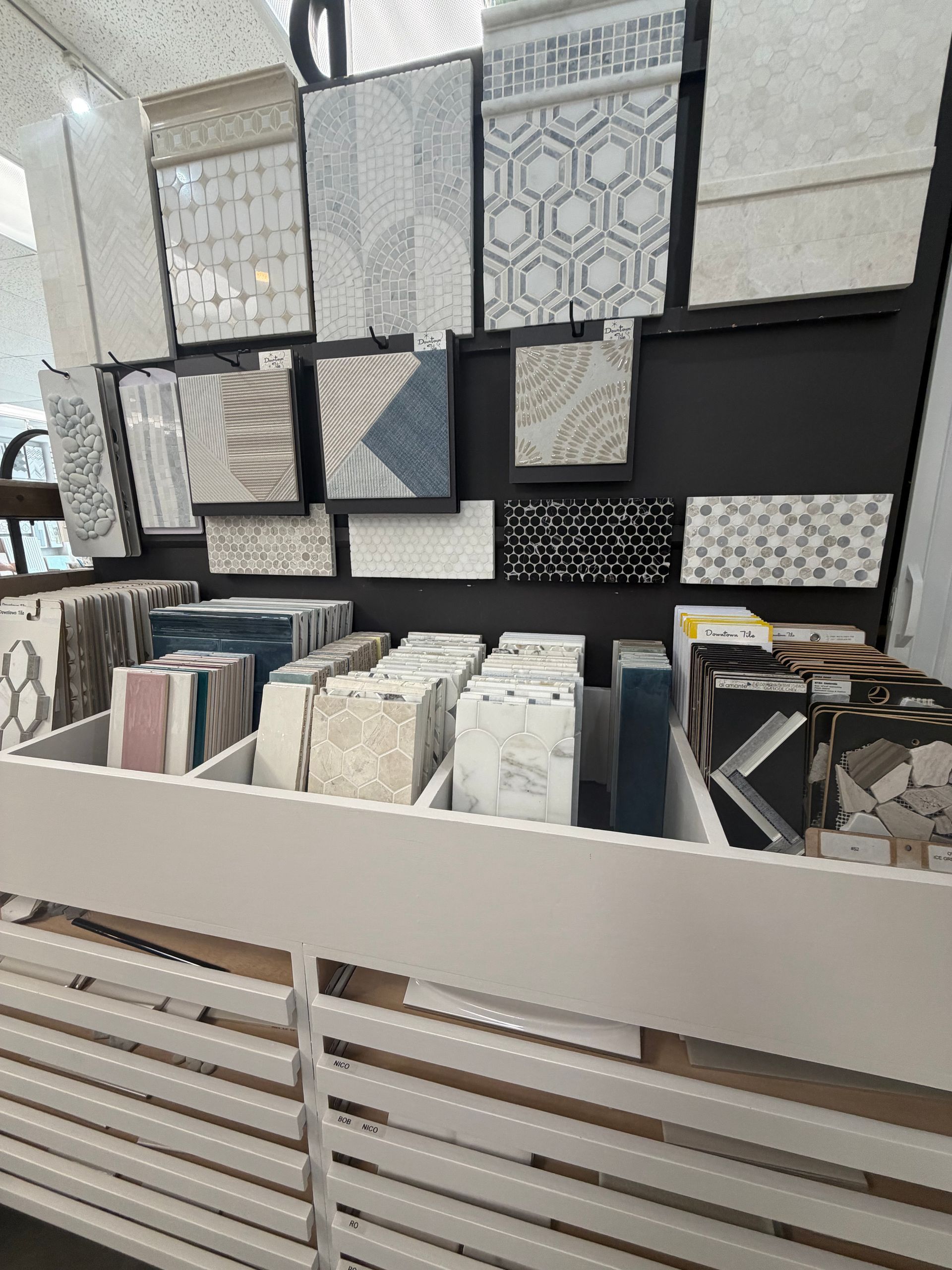 Tile display wall with patterned sample panels and bins of stone or ceramic tiles in a showroom