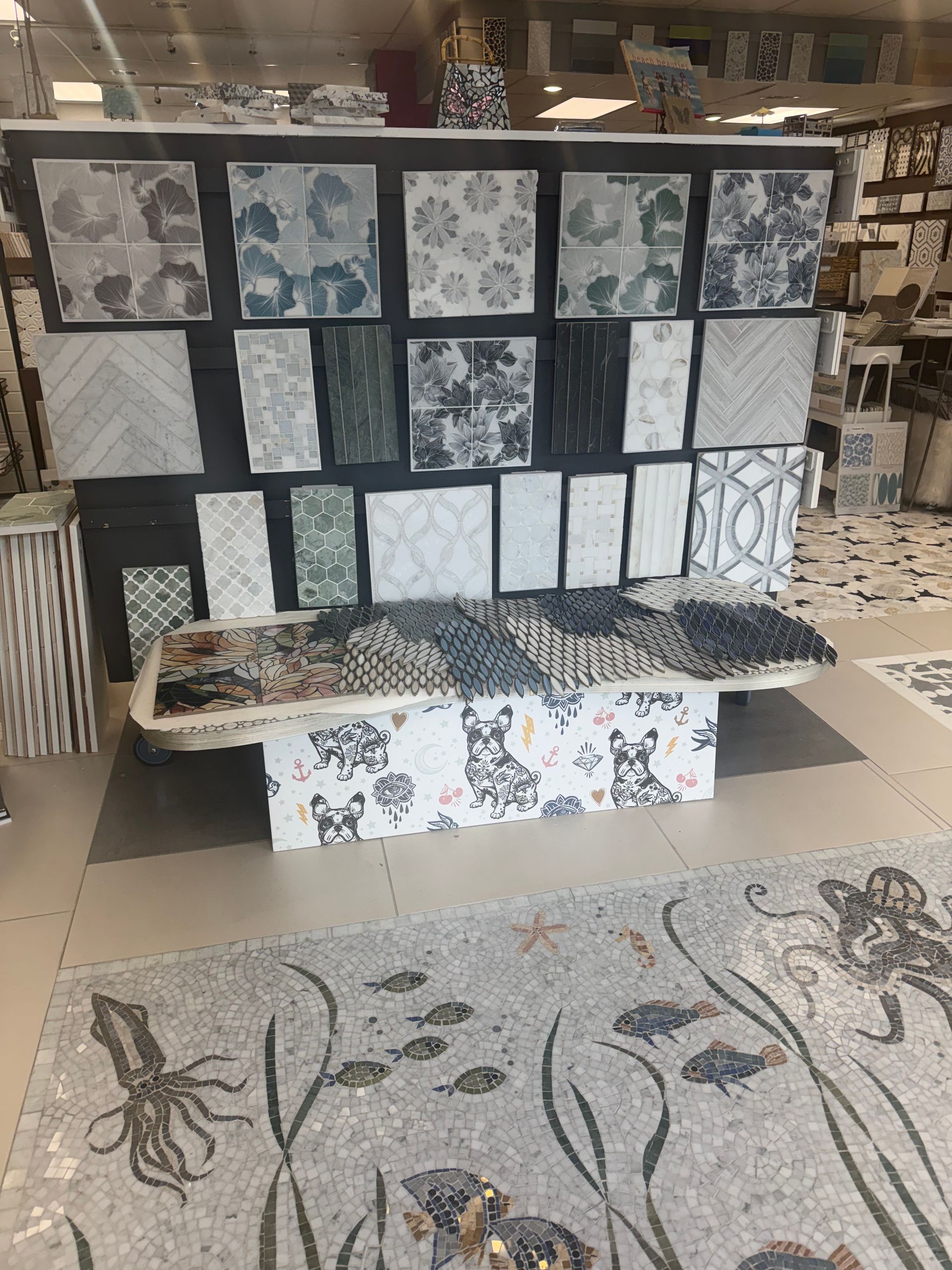Tile display with assorted black, white, and blue patterned tiles and a floral floor sample in a showroom