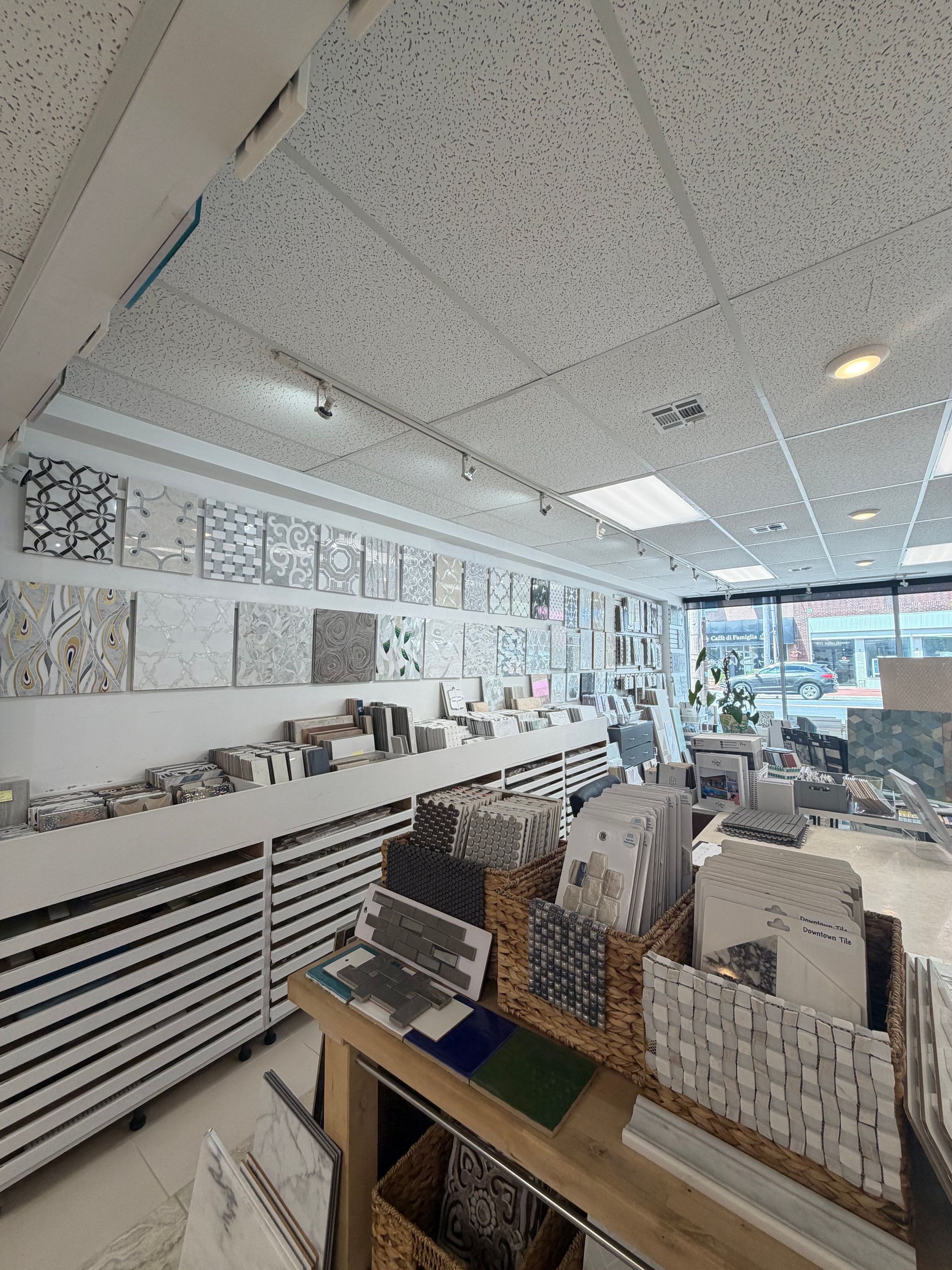 Bright retail store aisle with white patterned wall panels, display shelves, and boxed home decor items.