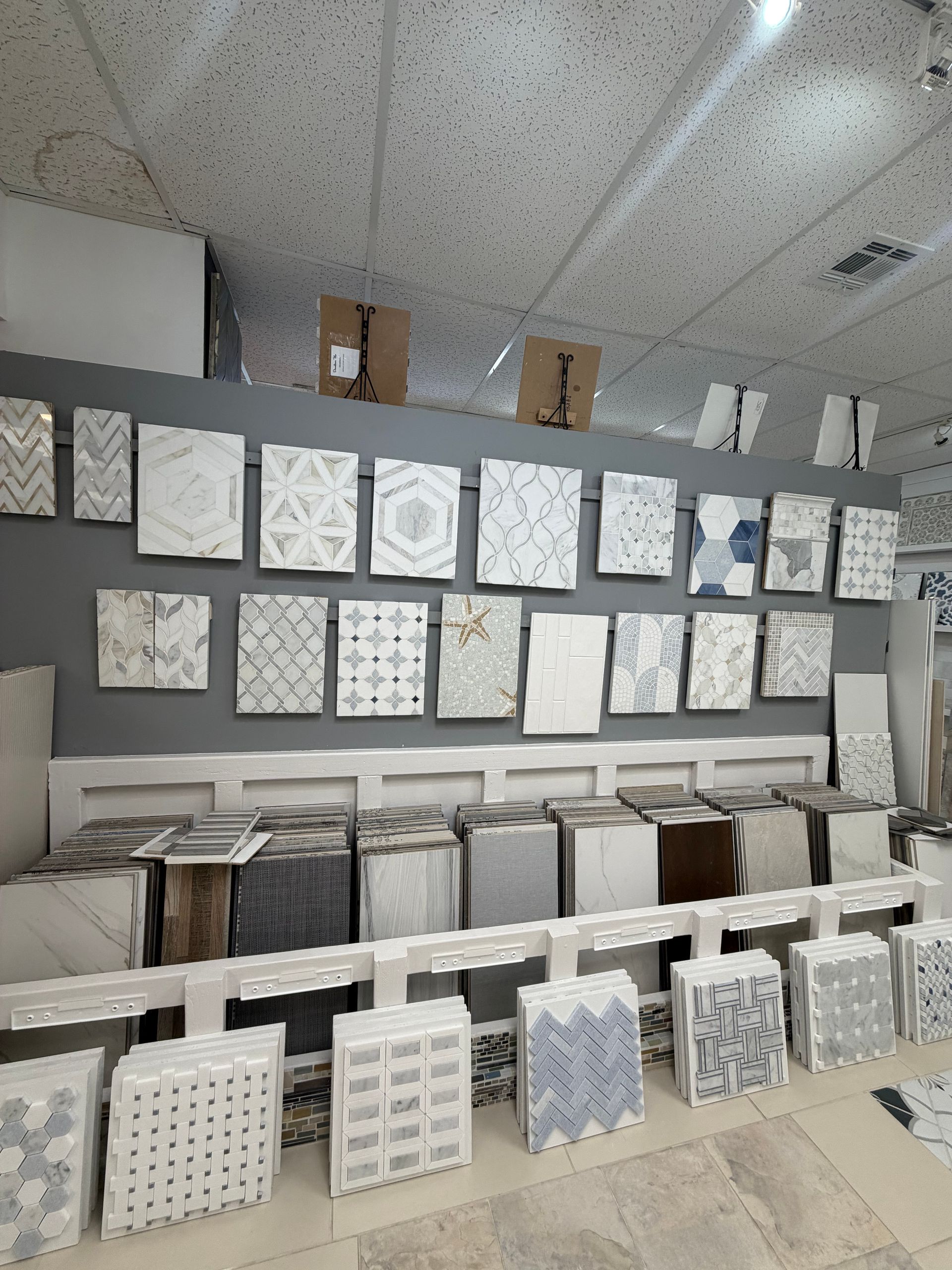 Store display of white patterned wall tiles arranged on shelves in a showroom.