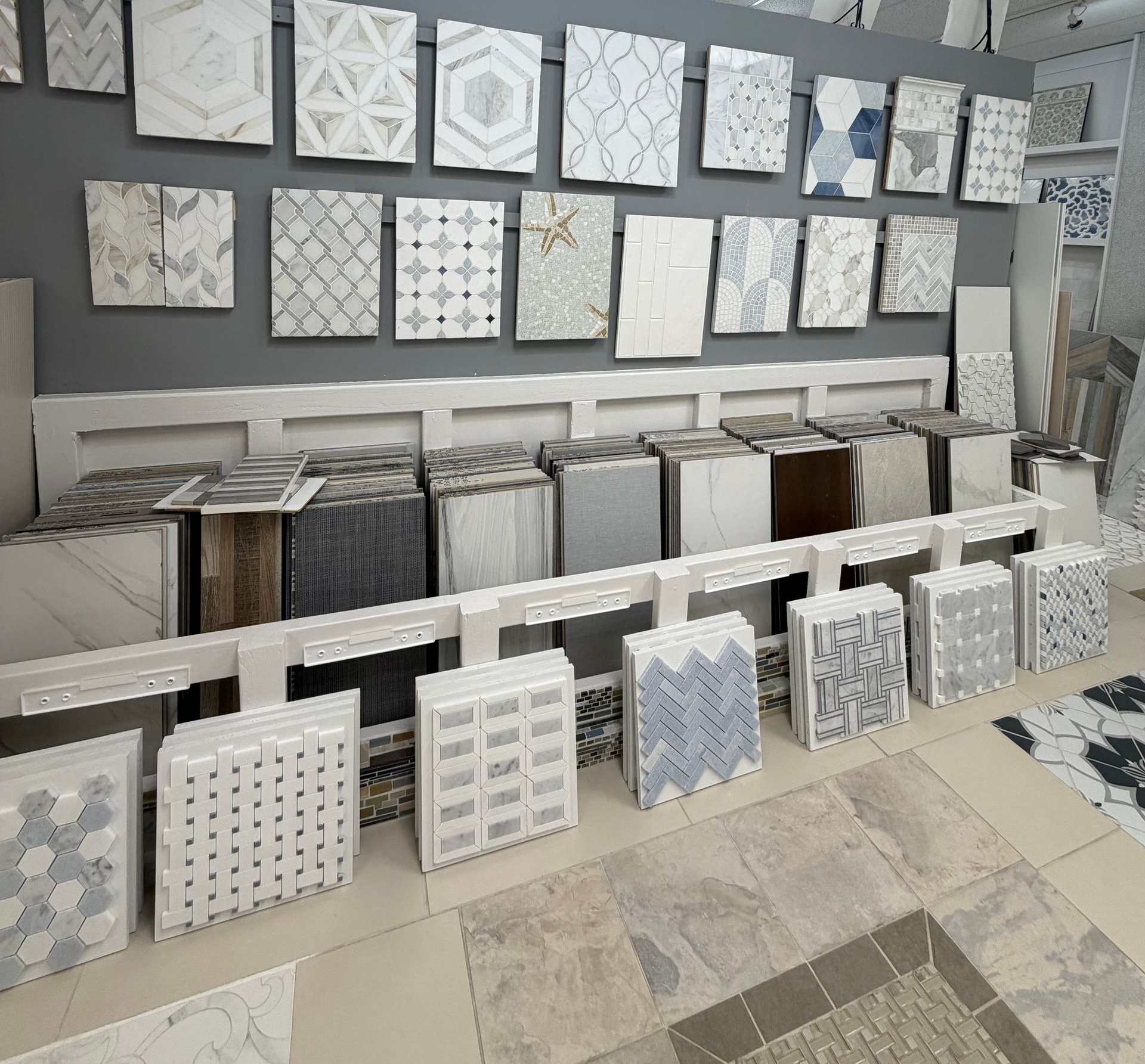Tile showroom wall with patterned white and gray tile samples displayed on shelves and stands