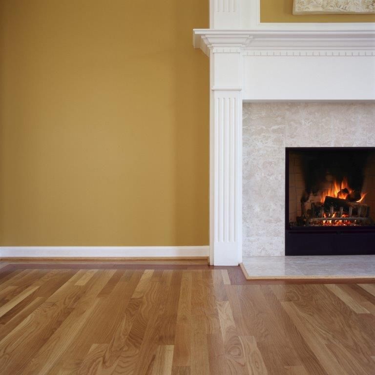 Wooden floor, yellow wall, and white fireplace. Fireplace lit with flames.