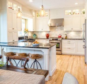 White kitchen with island, wooden stools, granite countertops, stainless steel appliances, and wood flooring.
