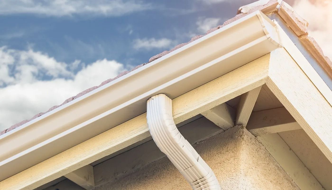 White downspout attached to the corner of a beige house roof under a cloudy sky