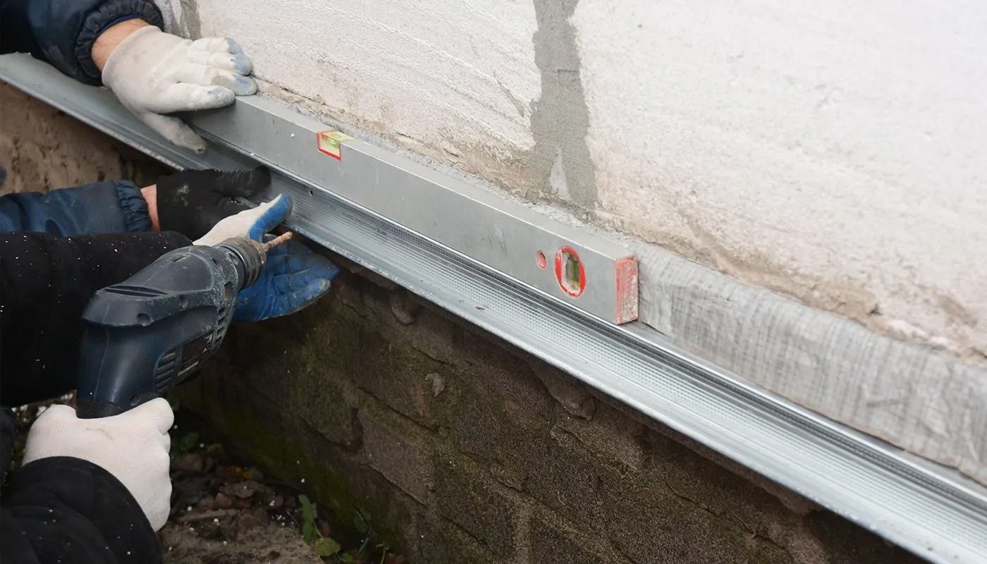 Hands installing a silver aluminum trim with a level against a white exterior wall.