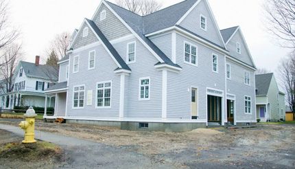 Gray house with white trim and multiple gables on a gravel lot, seen from the front-left side