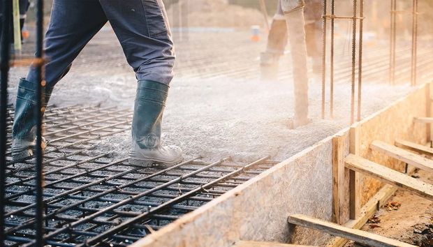 Worker pouring concrete into a rebar foundation at a construction site