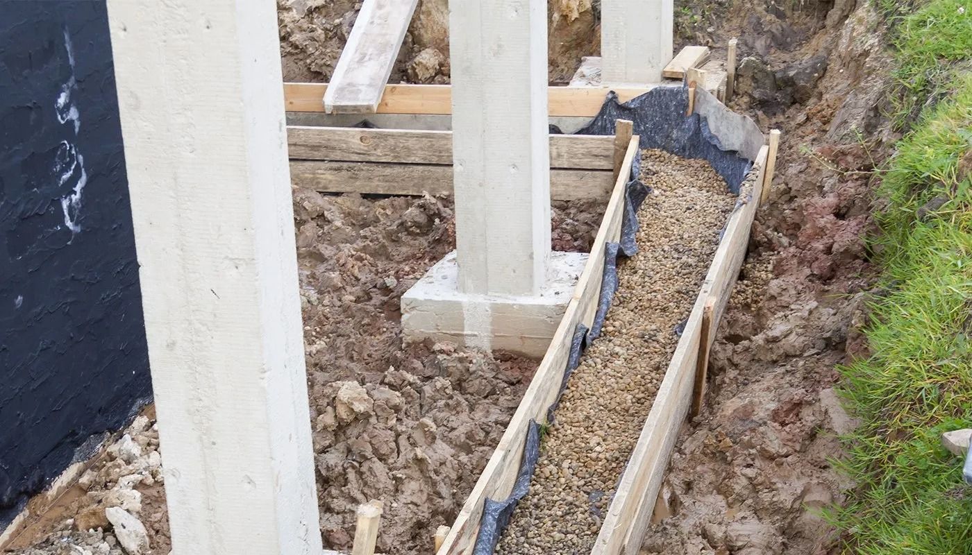 Construction site with concrete columns and a narrow gravel trench beside a building foundation