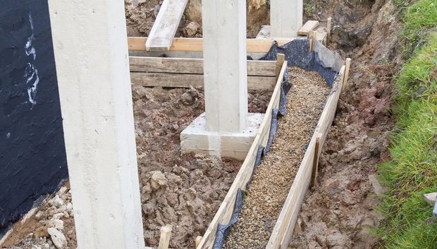 Construction site with concrete columns and a trench filled with gravel beside a foundation wall