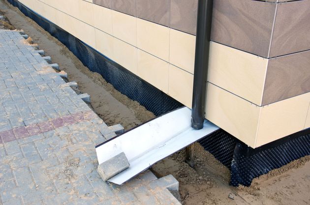White drainage pipe extending from a building wall onto a paved slope near stairs