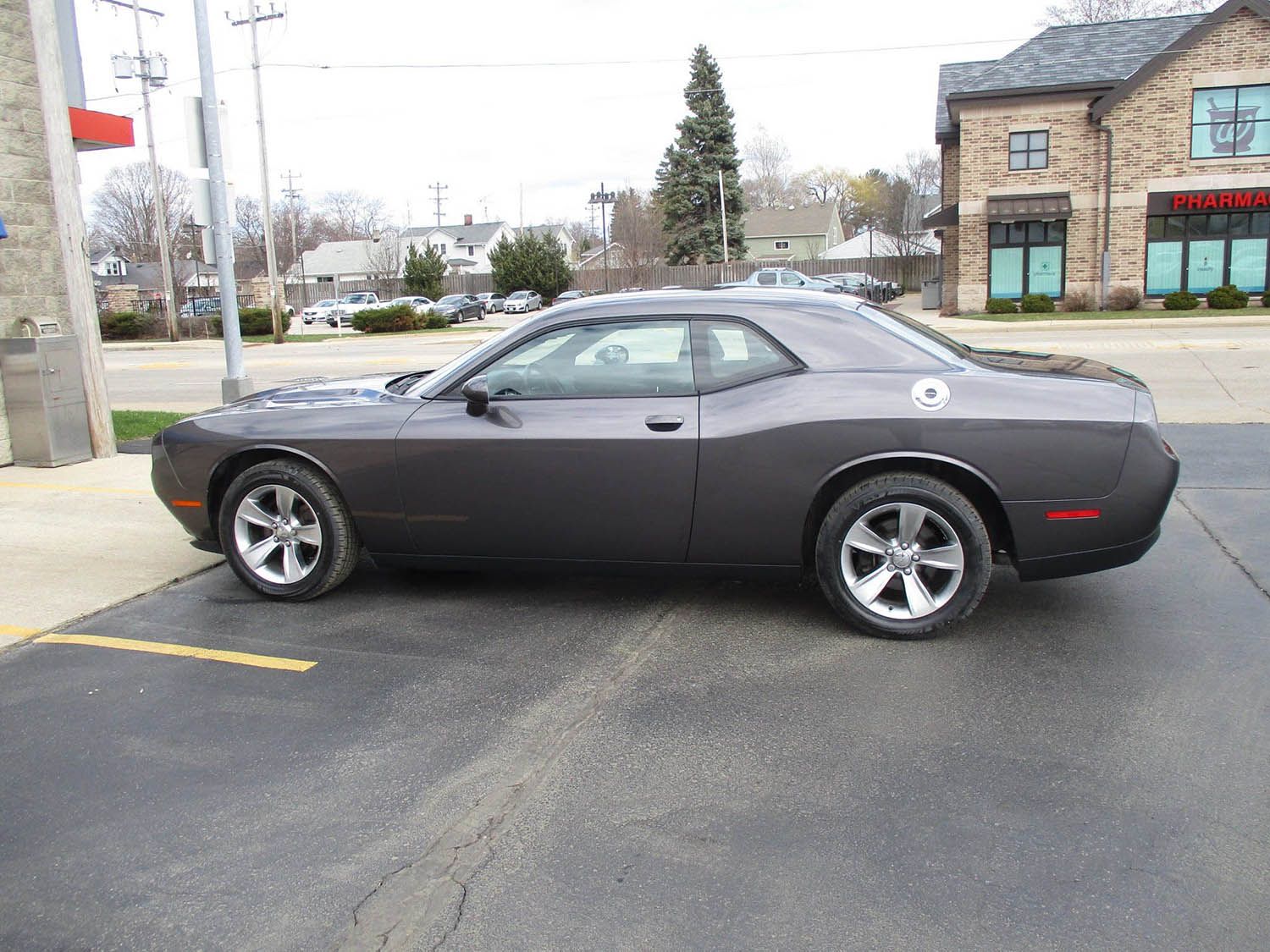 A gray dodge challenger is parked in a parking lot in front of a building.