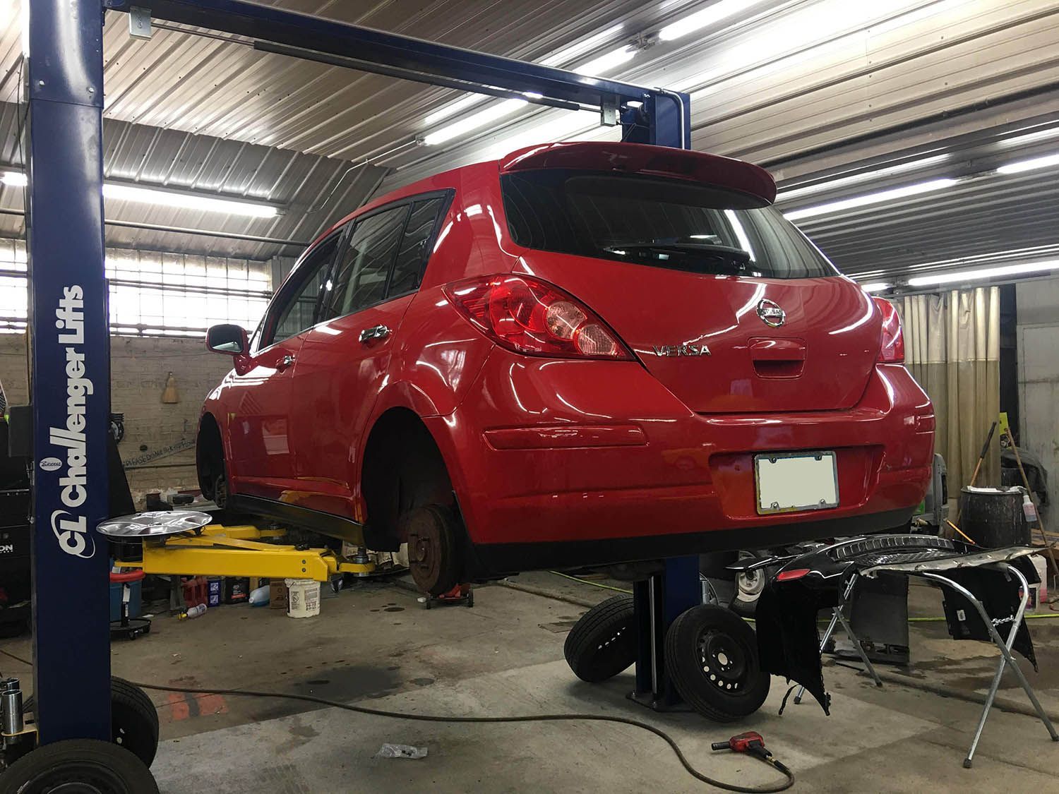 A red car is sitting on a lift in a garage.