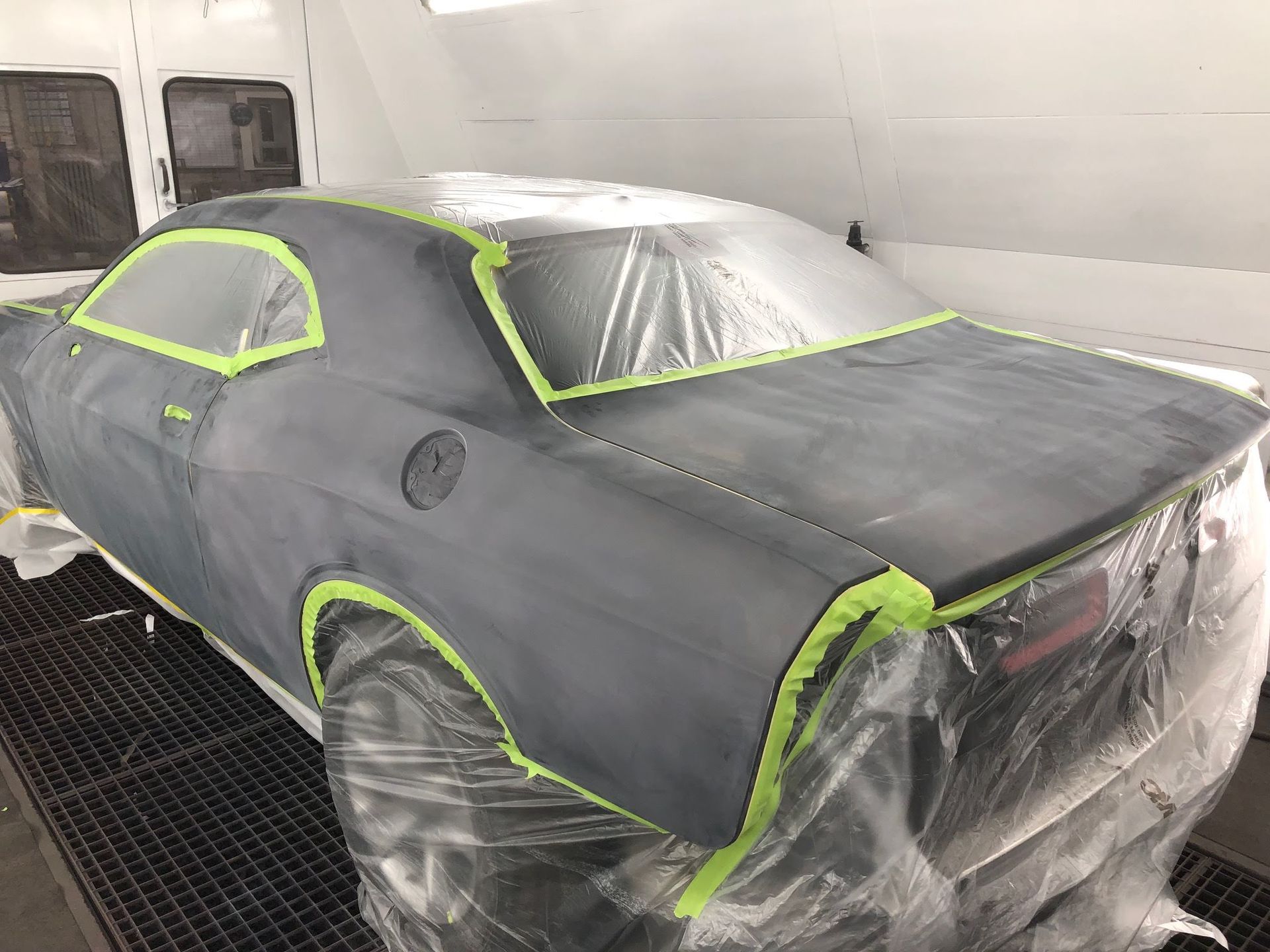 A dodge challenger is being painted in a paint booth.