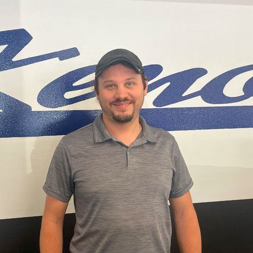 A man wearing a hat and a gray shirt is standing in front of a sign.