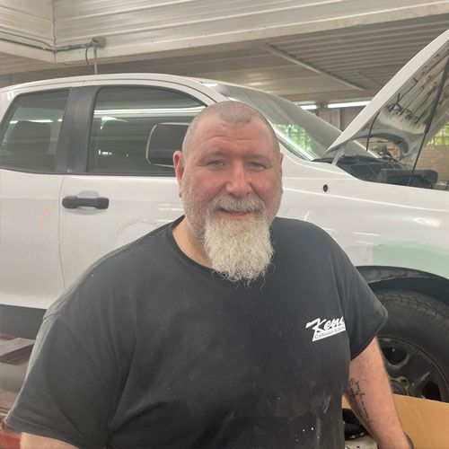 A man with a beard is standing in front of a white truck.
