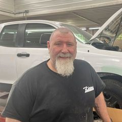 A man with a beard is standing in front of a white truck.