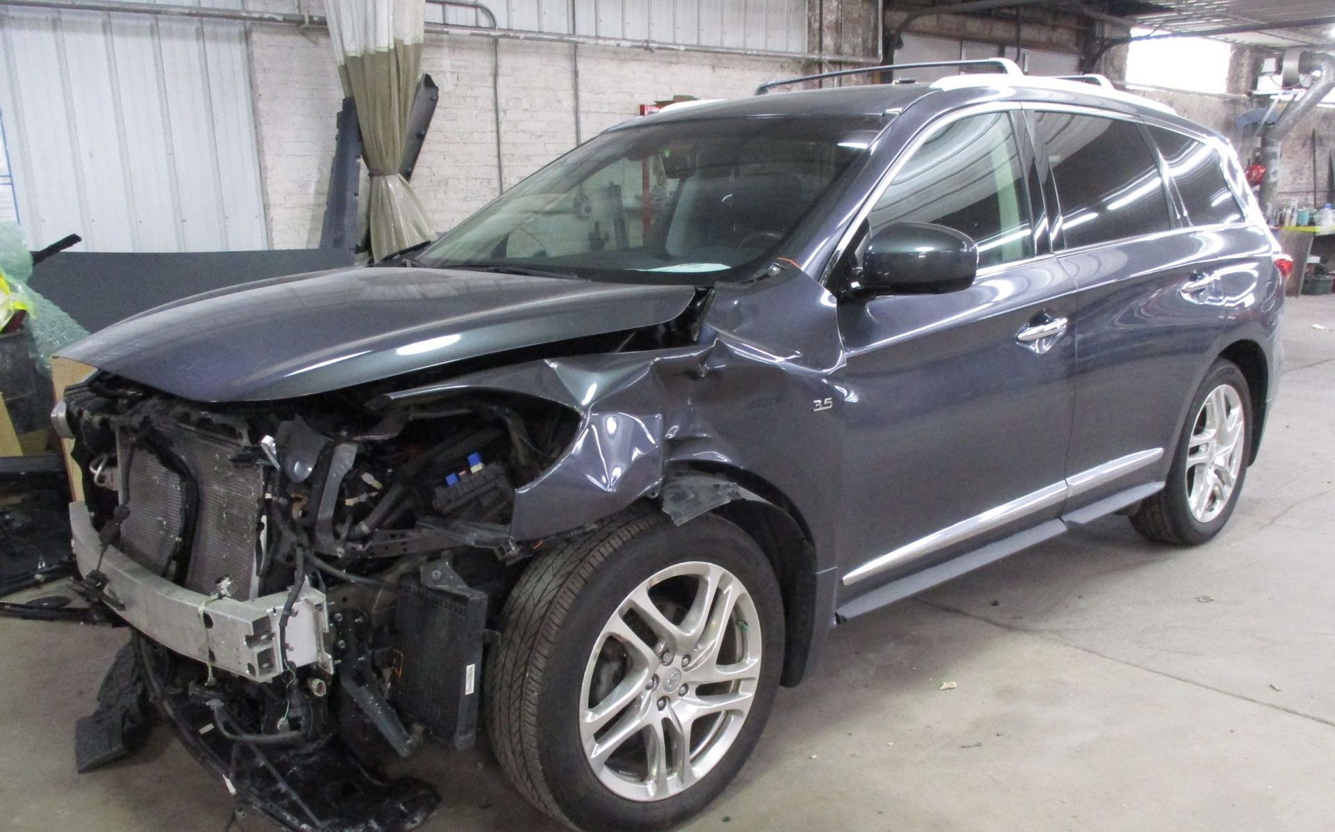 A gray suv with a damaged front end is sitting in a garage.