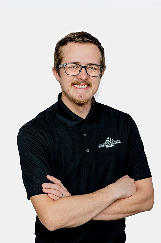 A man wearing glasses and a black shirt is standing with his arms crossed.