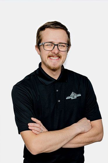 A man wearing glasses and a black shirt is standing with his arms crossed.