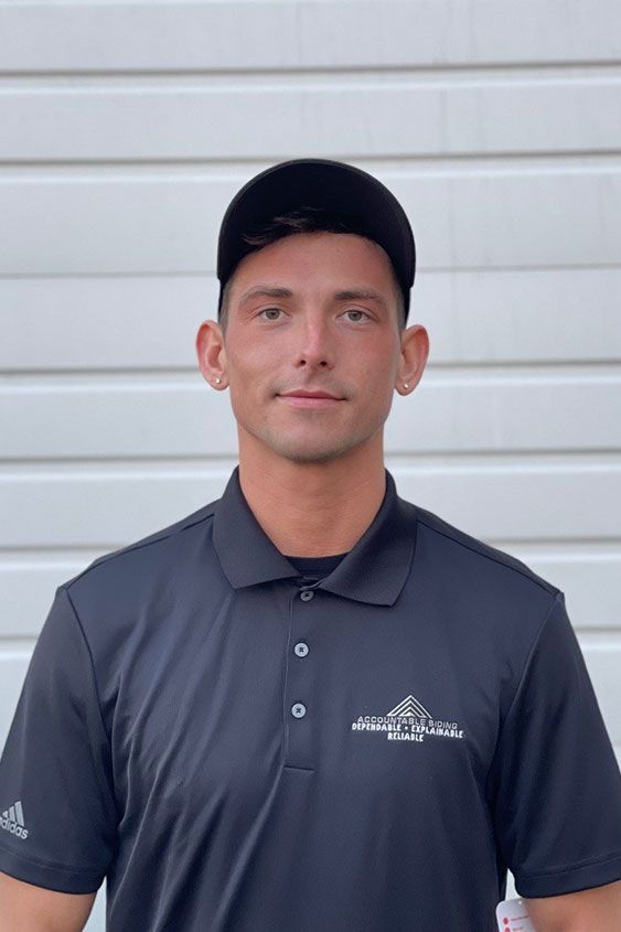 A man wearing a black polo shirt and a black hat is standing in front of a garage door.