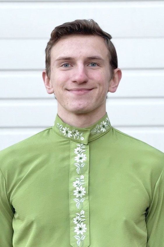 A young man wearing a green shirt and tie is smiling.