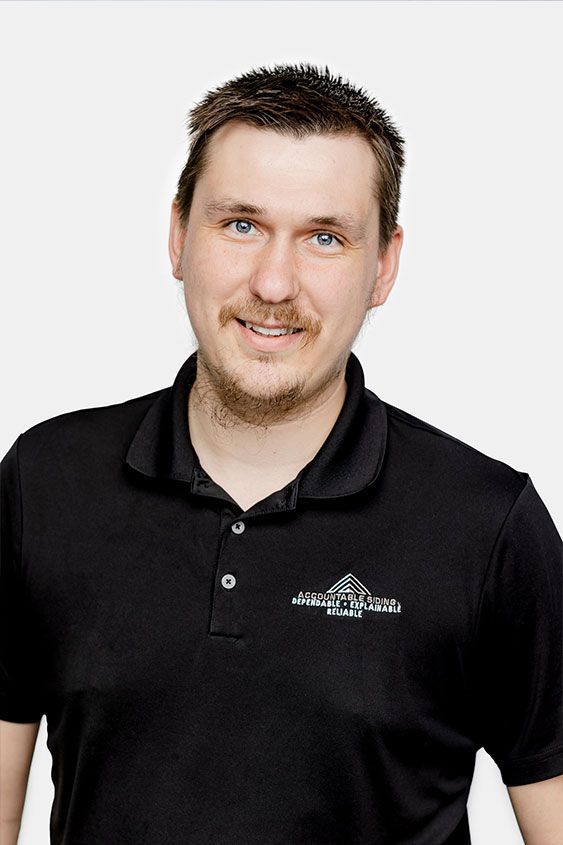 A man with a beard is wearing a black polo shirt and smiling.