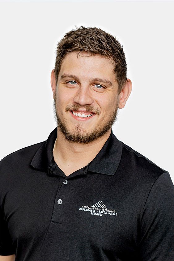 A man with a beard is wearing a black polo shirt and smiling.