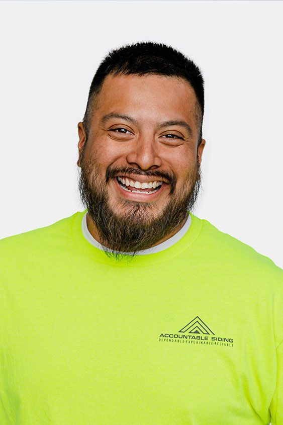 A man with a beard is wearing a neon yellow shirt and smiling.