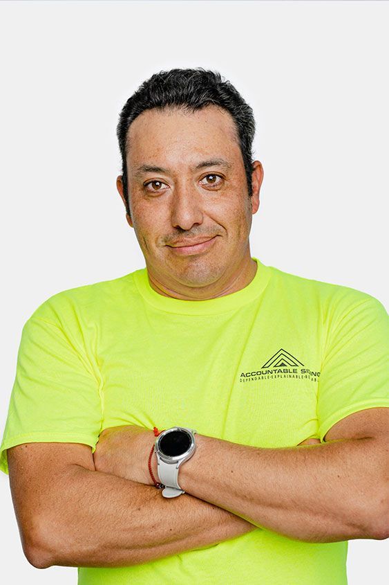 A man wearing a neon yellow t-shirt and a watch is standing with his arms crossed.