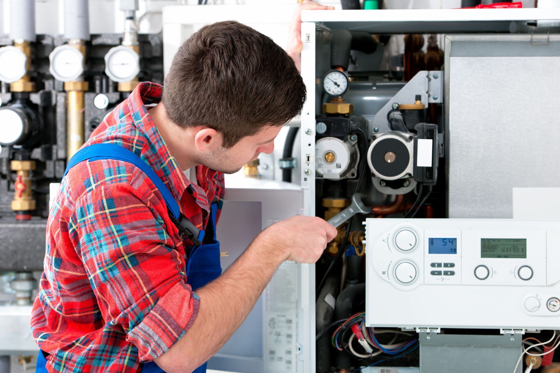 Technician inspecting an open boiler unit with tools and wiring visible indoors