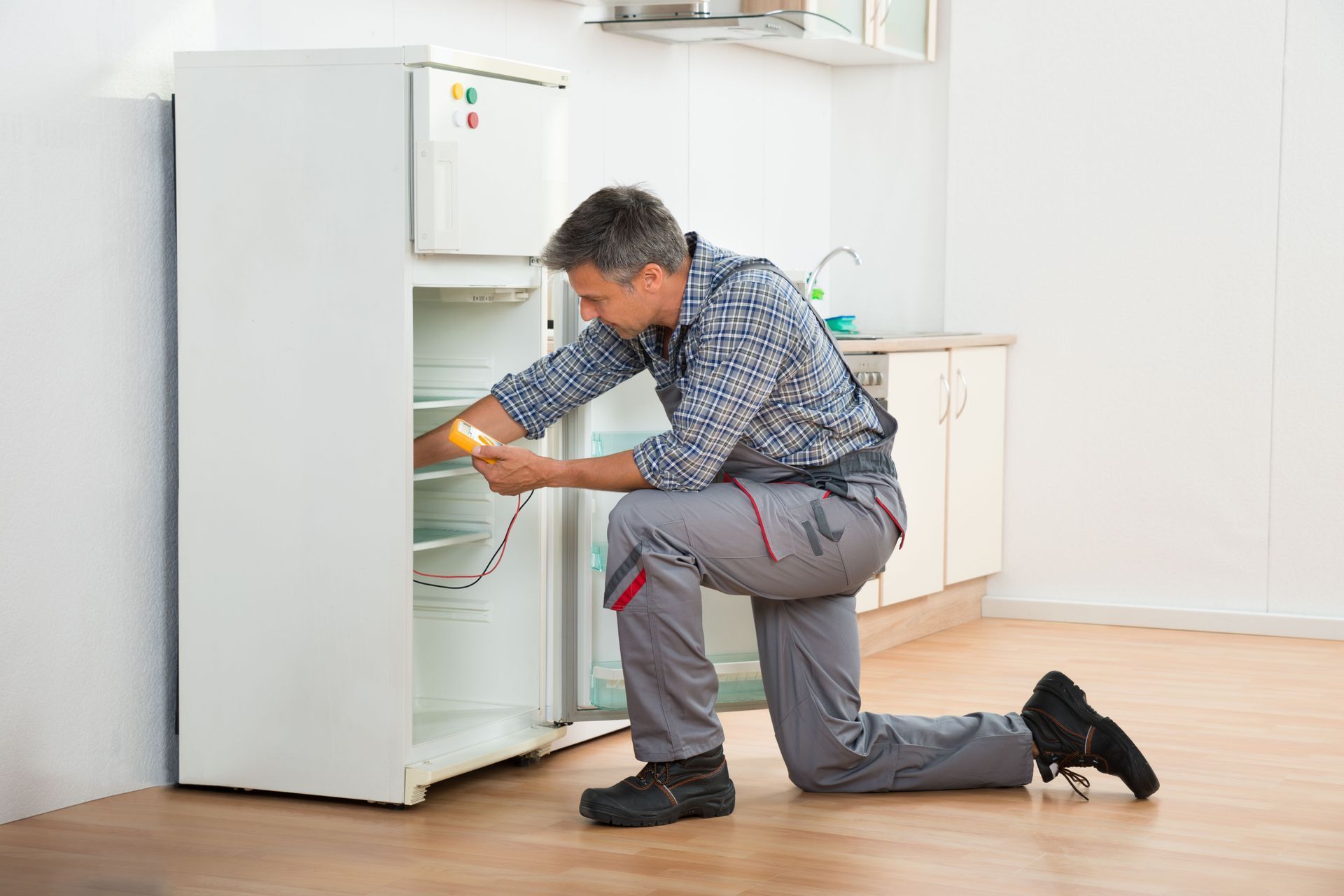 Man kneels on kitchen floor, loading food into an open refrigerator.