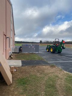 Outdoor lot beside a building with a green tractor parked near gray barriers under cloudy skies