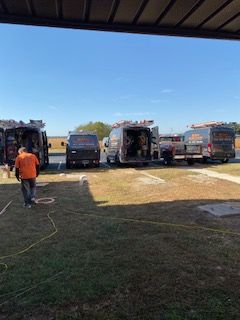 Parked garbage trucks in a lot with one worker in an orange shirt walking in the foreground.