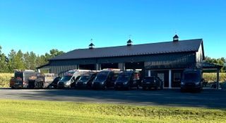 Black pickup trucks parked beside a long barn-style building on a sunny rural lot