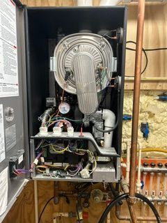 Open HVAC furnace cabinet with exposed blower, wiring, and pipes in a basement.