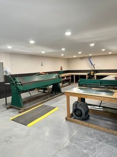 Large workshop with green industrial machinery, tables, and overhead lights on a concrete floor