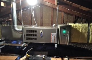 Attic HVAC unit with metal ductwork and a green indicator light beside insulation and rafters