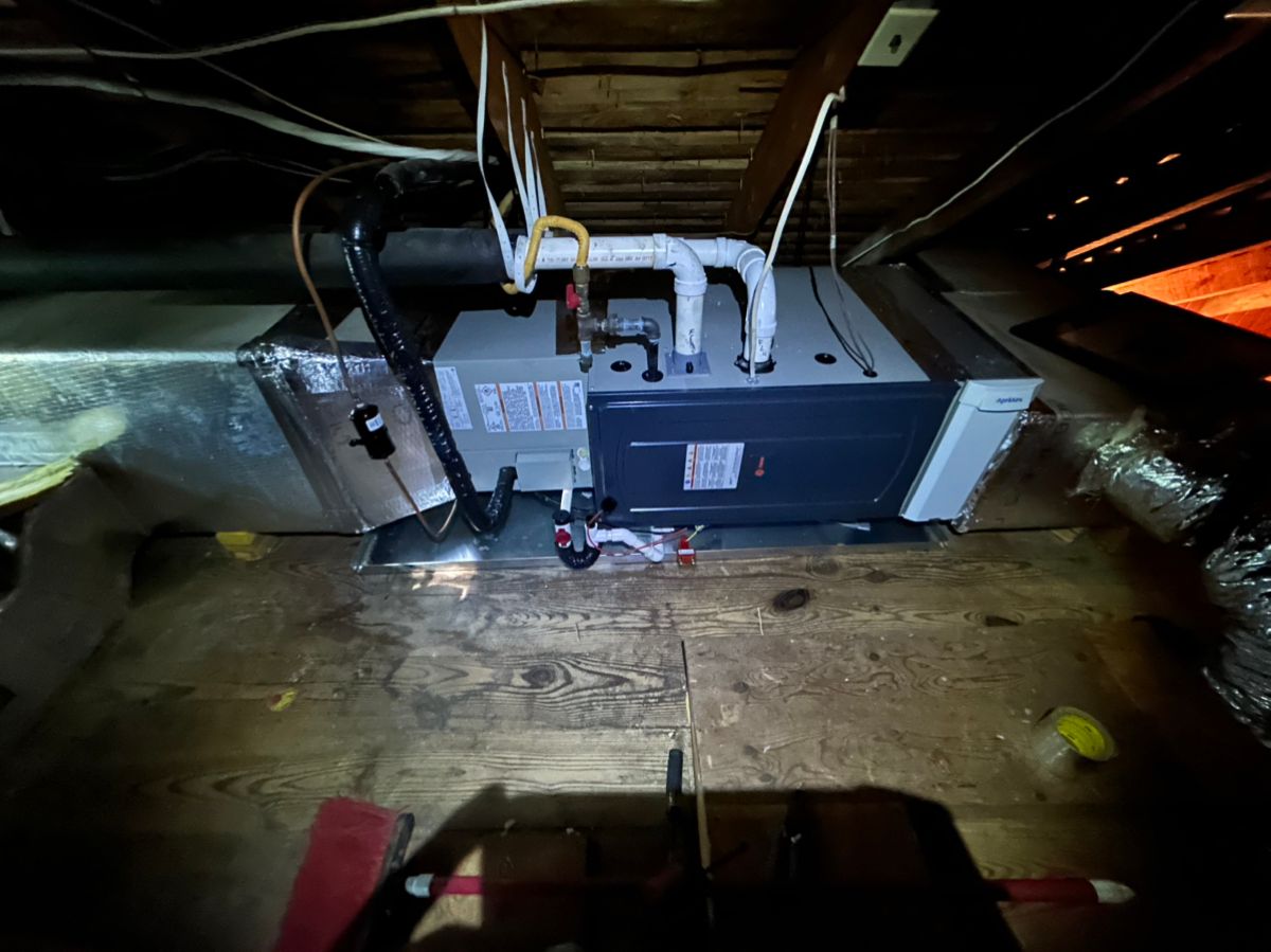 Air handler unit in a cramped attic with exposed wooden beams and ductwork