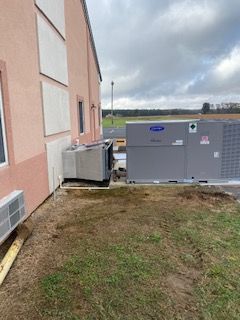 Outdoor HVAC units beside a peach building, with grassy ground and a cloudy field in the background