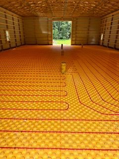 Large room with orange floor heating pipes laid in loops and a doorway opening to greenery.