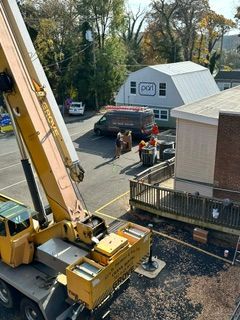 Workers beside a yellow crane lift equipment near a house in a parking lot
