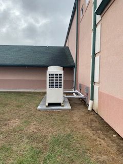 Portable air conditioner beside a pink building wall on a grassy lawn under cloudy sky