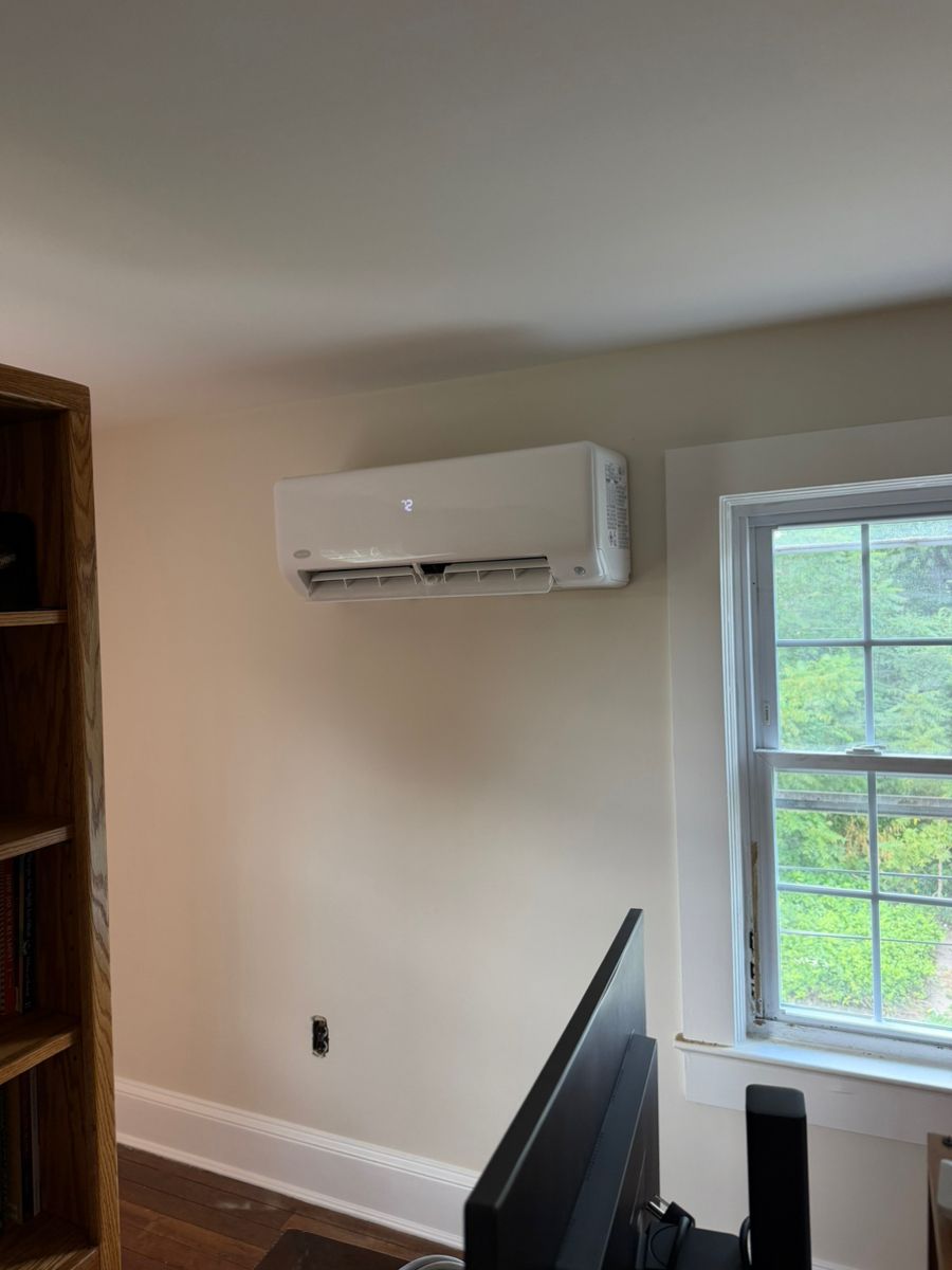 Home office with wall-mounted air conditioner beside a window and computer monitor in the foreground