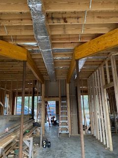 Unfinished interior with exposed framing, ceiling ductwork, and ladders in a narrow room under construction