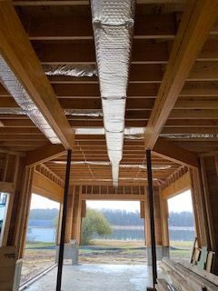 Interior of a wood-framed porch under construction, with exposed beams and silver HVAC ducts overhead.