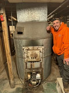 Person in orange hoodie standing beside a large gray furnace in a basement.