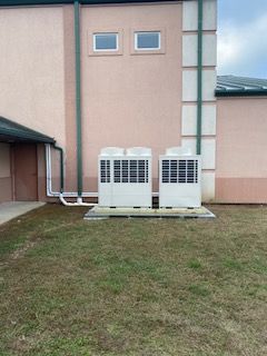 Two white outdoor HVAC units beside a pink building on a grassy lawn.
