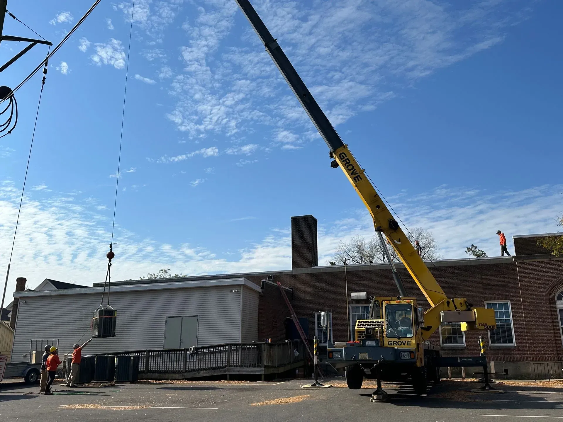 Roof workers on a building with a yellow crane lifting materials under a blue sky